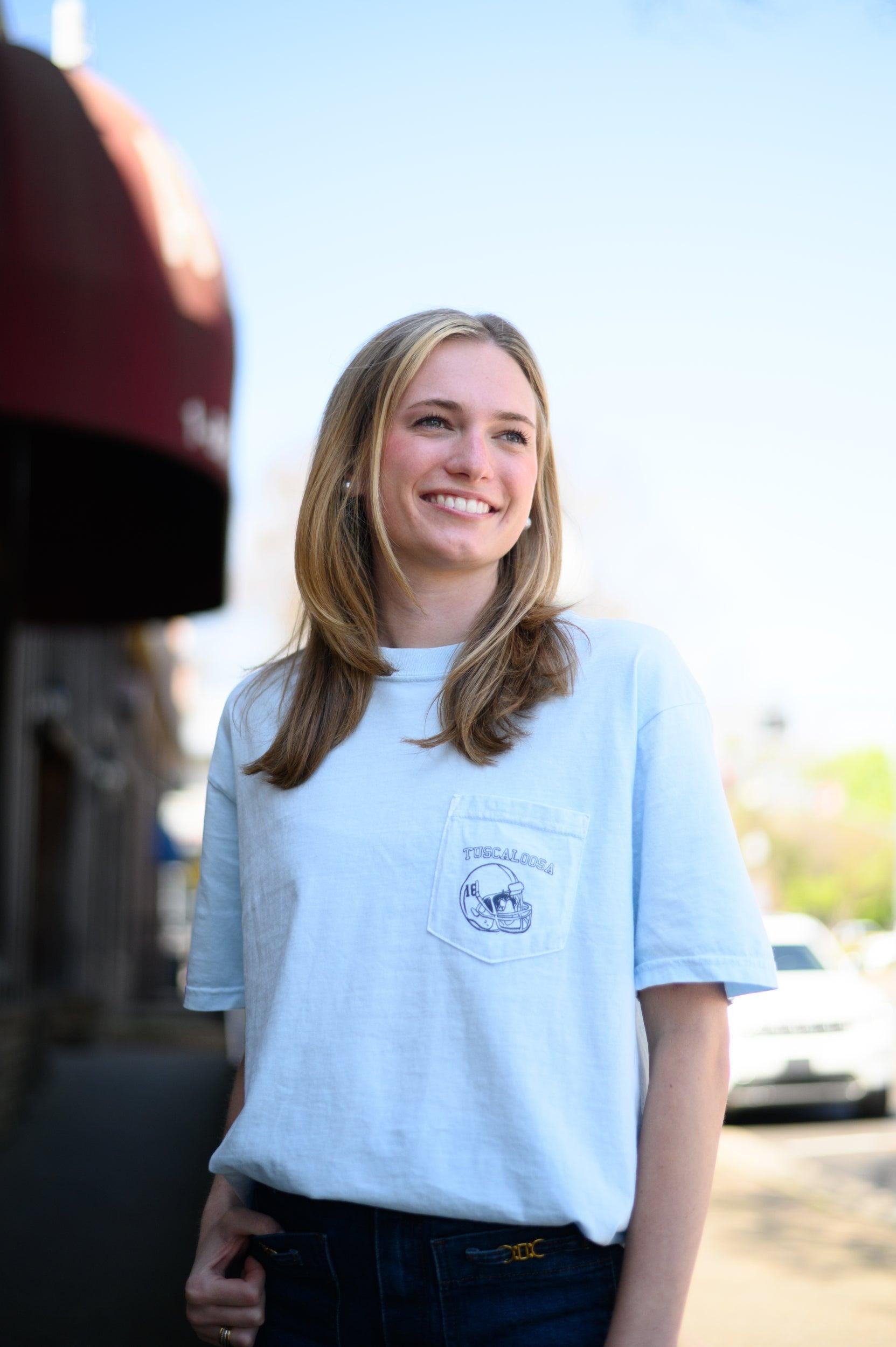 Local Merch Light Blue T-Shirt with a front pocket design featuring a football helmet and text “Tuscaloosa”