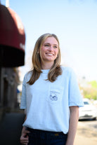 Local Merch Light Blue T-Shirt with a front pocket design featuring a football helmet and text “Tuscaloosa”