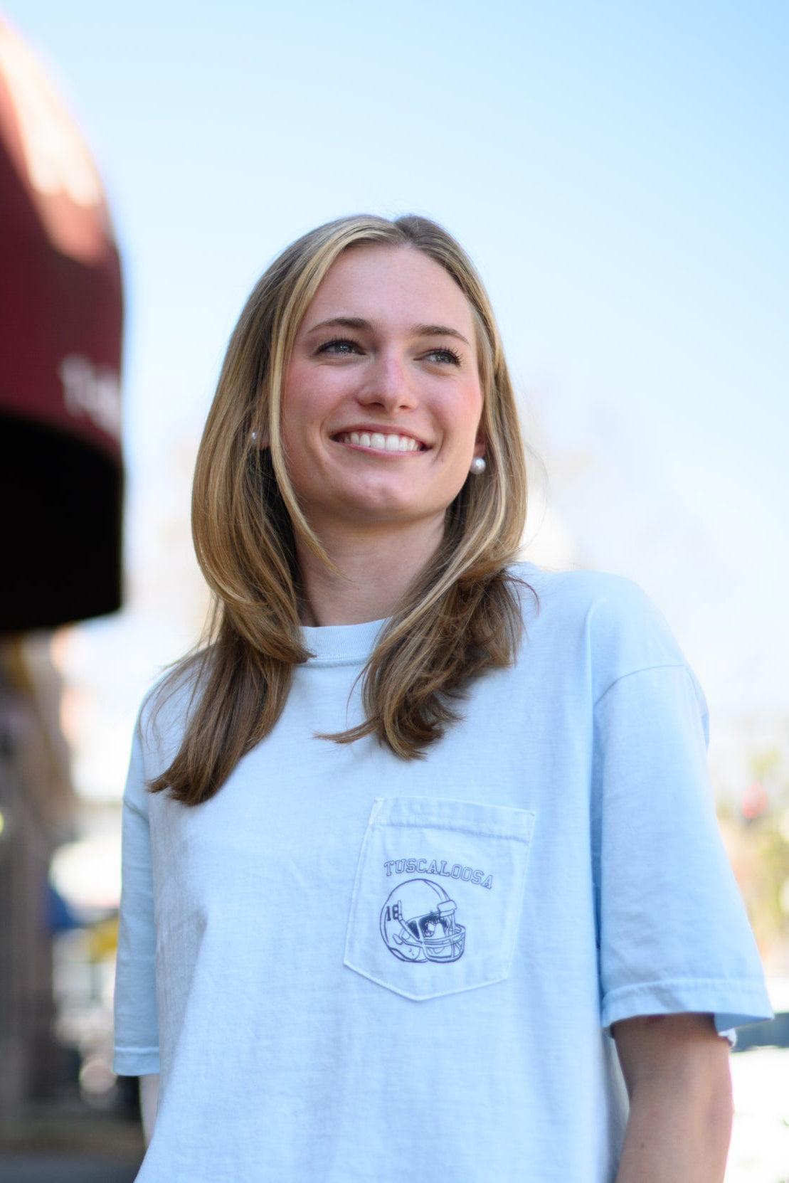 Local Merch Light Blue T-Shirt with a front pocket design featuring a football helmet and text “Tuscaloosa”
