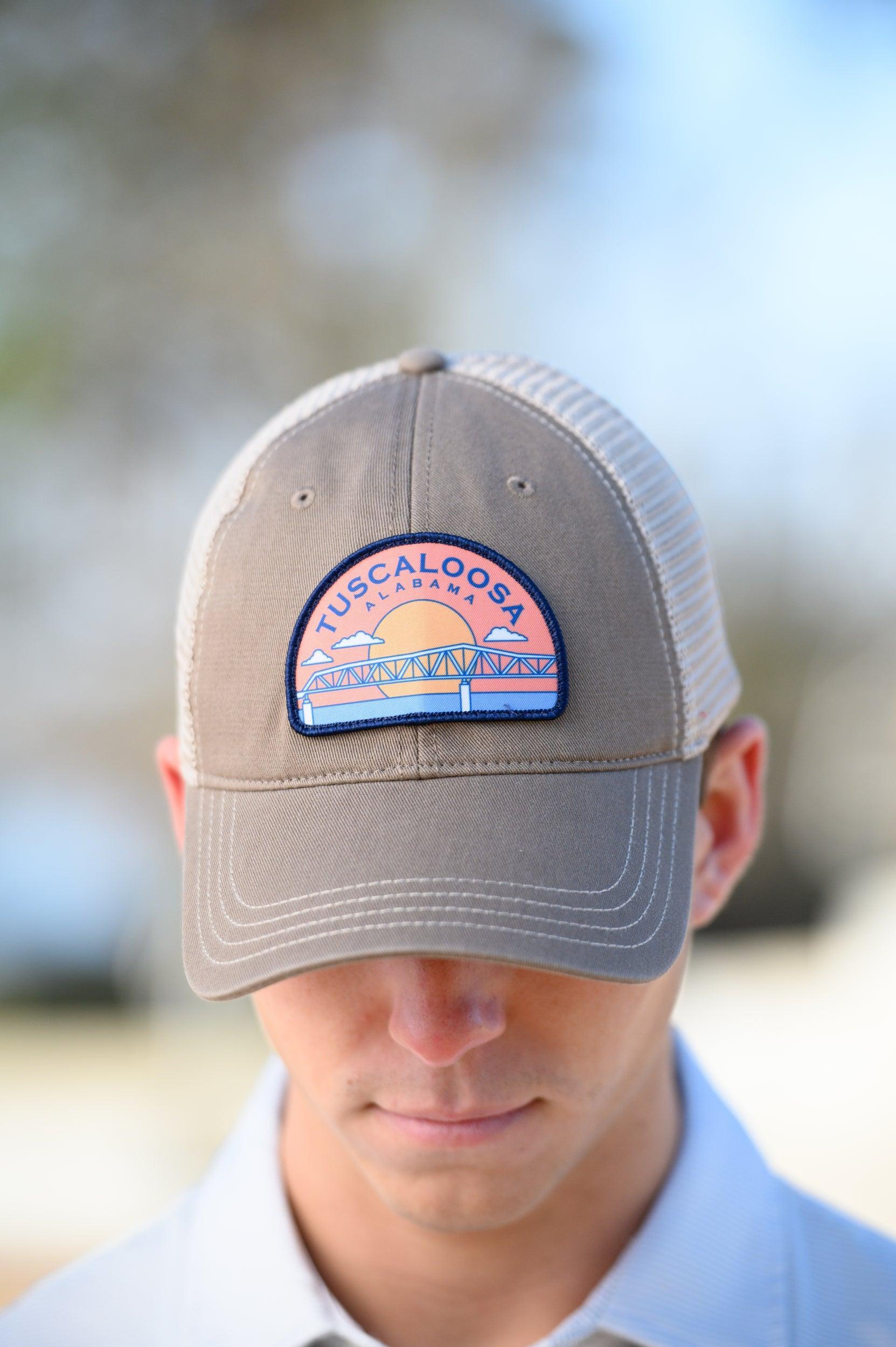 Tuscaloosa Beige Trucker Hat with a patch featuring Navy text "Tuscaloosa Alabama" a drawing of the sun setting on the iconic Tuscaloosa Trestle