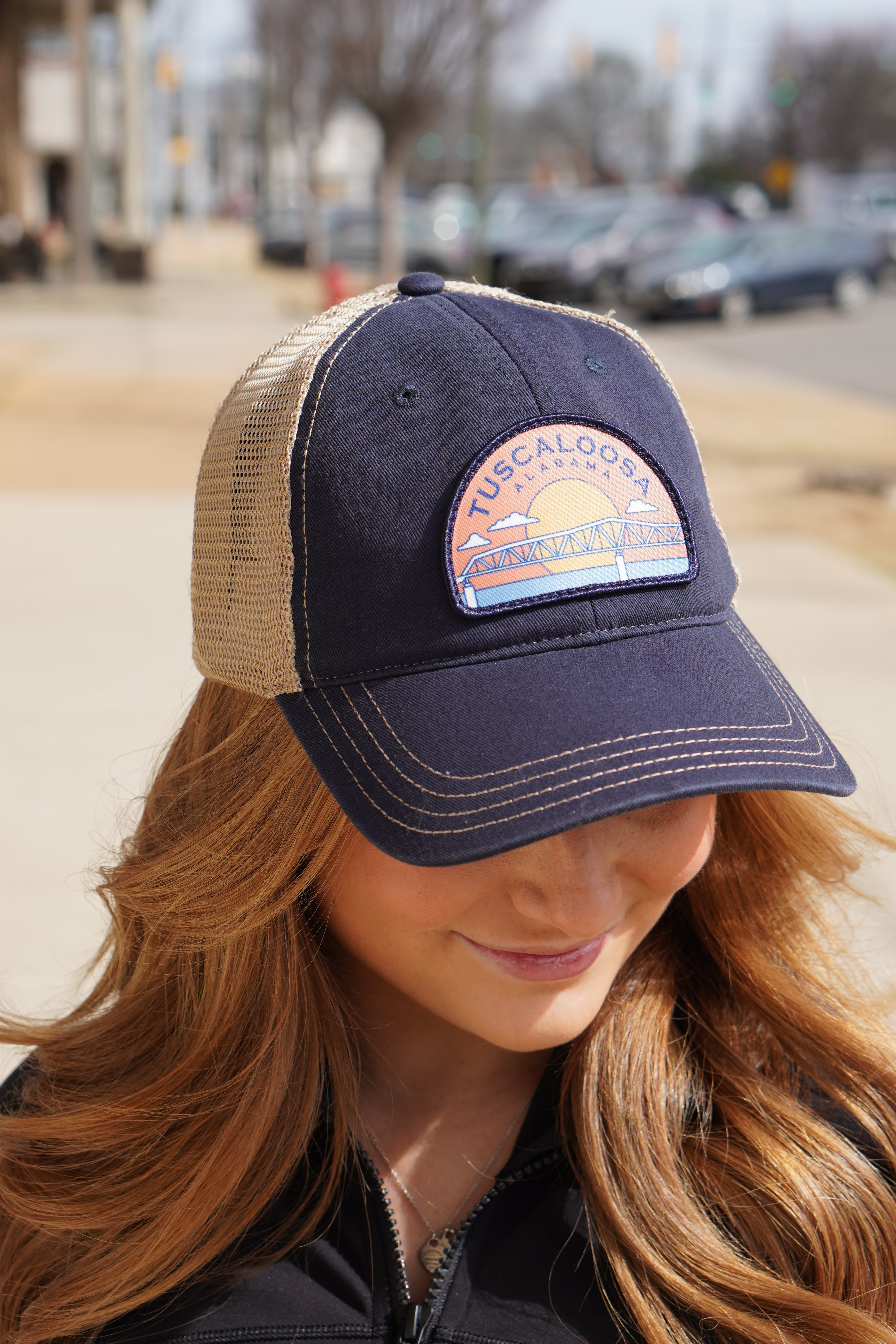 Tuscaloosa Navy and Beige Trucker Hat with a patch featuring Blue text "Tuscaloosa Alabama" a drawing of the sun setting on the iconic Tuscaloosa Railroad Tracks 