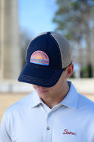 Tuscaloosa Navy and Beige Trucker Hat with a patch featuring Navy text "Tuscaloosa Alabama" a drawing of the sun setting on the iconic Tuscaloosa Railroad Tracks