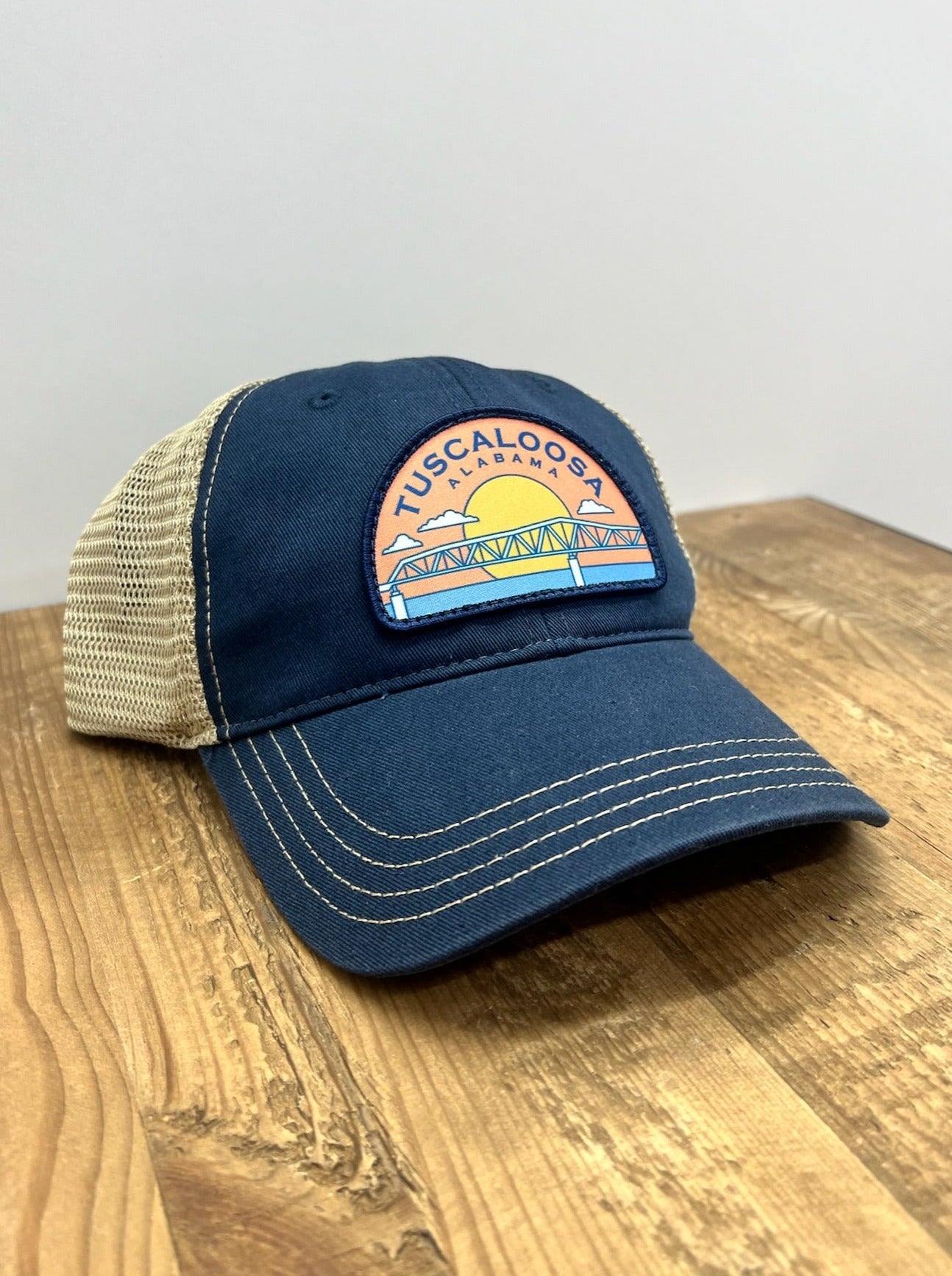 Tuscaloosa Navy and Beige Trucker Hat with a patch featuring Blue text "Tuscaloosa Alabama" a drawing of the sun setting on the iconic Tuscaloosa Railroad Tracks 