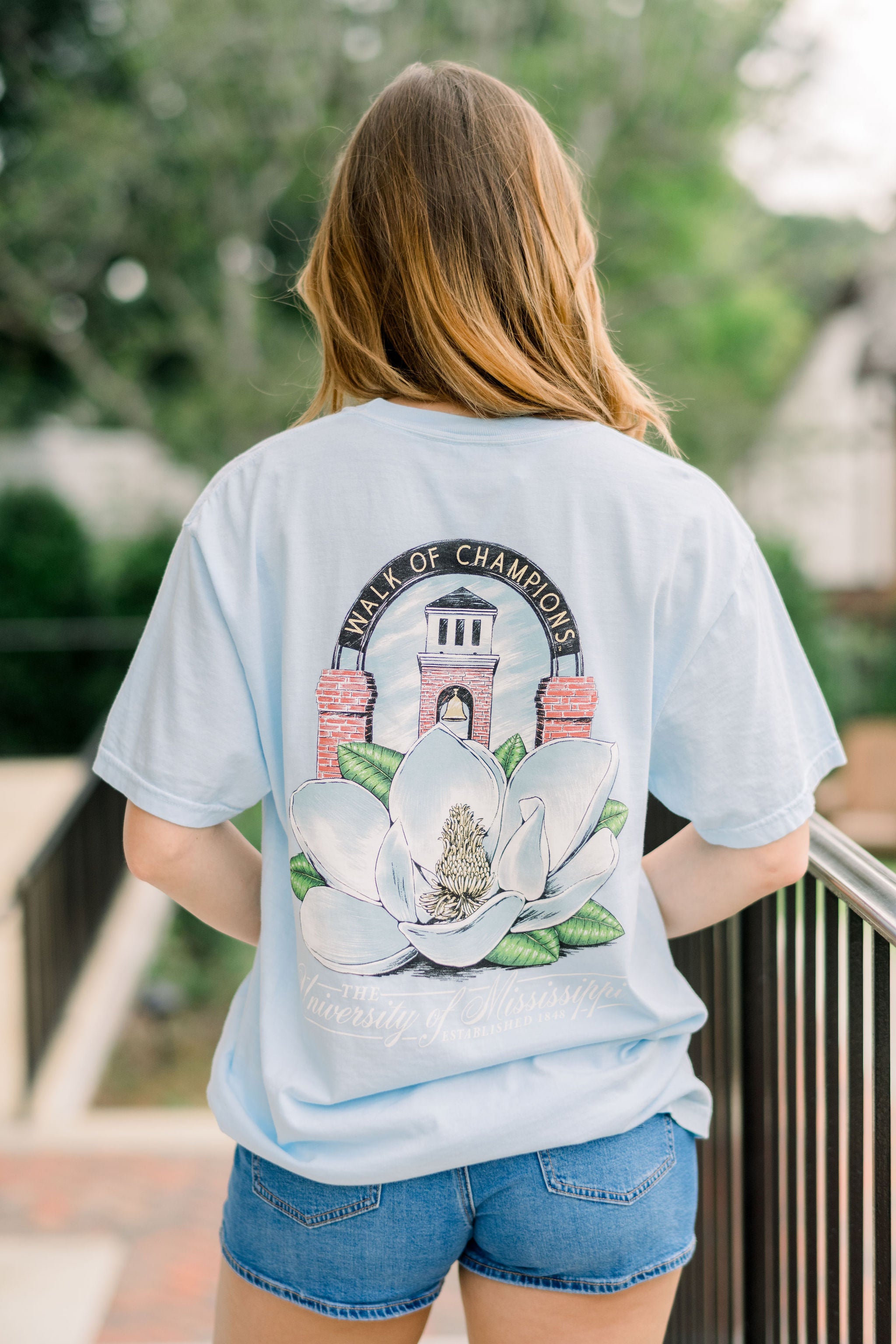 Light blue t-shirt with a magnolia flower graphic and 'University of Mississippi' text on a white background