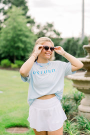 Ole Miss Light Blue T-Shirt with Electric Blue Text on the front, “OXFORD.” The Back features sketches of Oxford Icons such as the Walk of Champions Gate, The Vaught stadium, and the Lyceum 