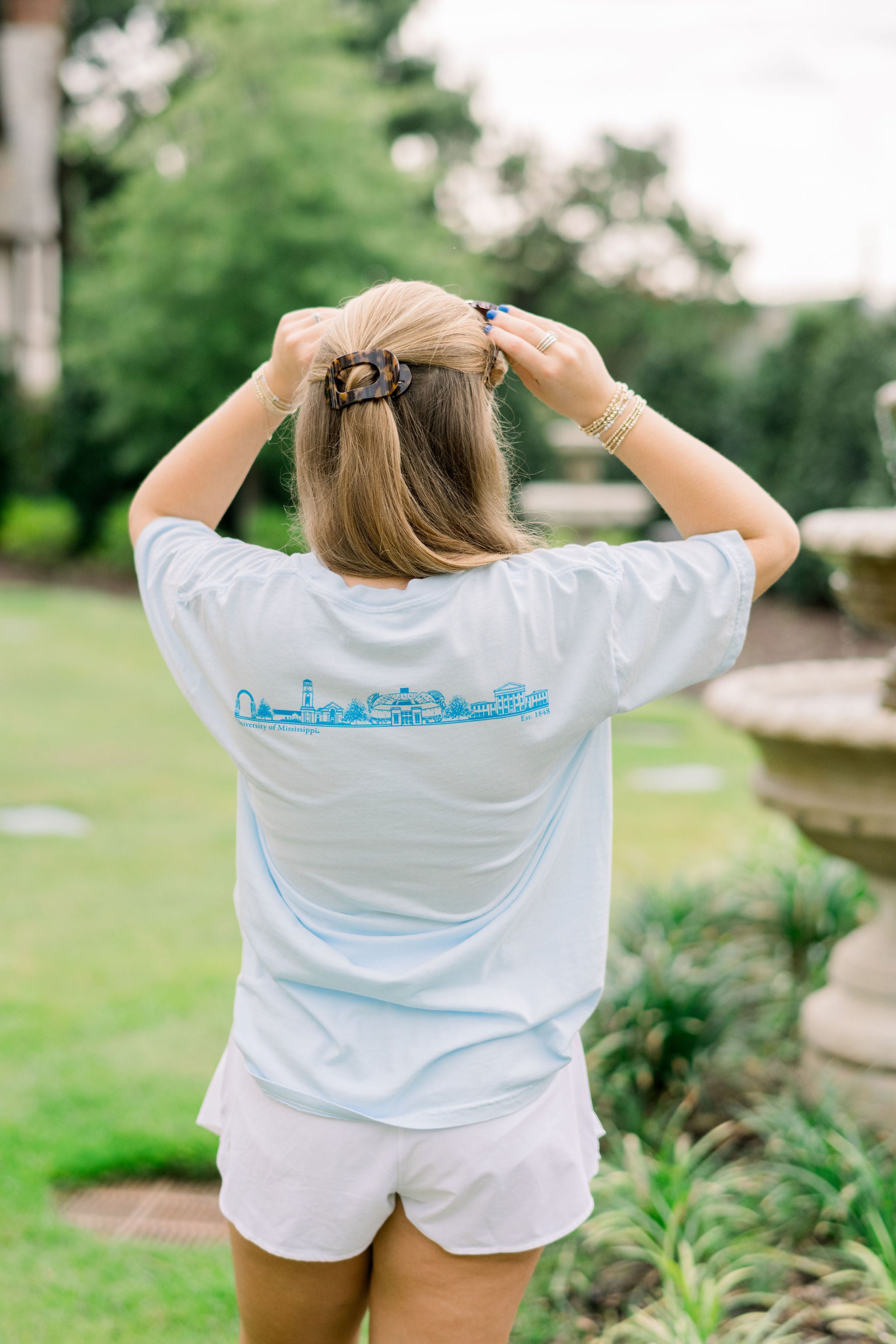 Ole Miss Light Blue T-Shirt with Electric Blue Text on the front, “OXFORD.” The Back features sketches of Oxford Icons such as the Walk of Champions Gate, The Vaught stadium, and the Lyceum 