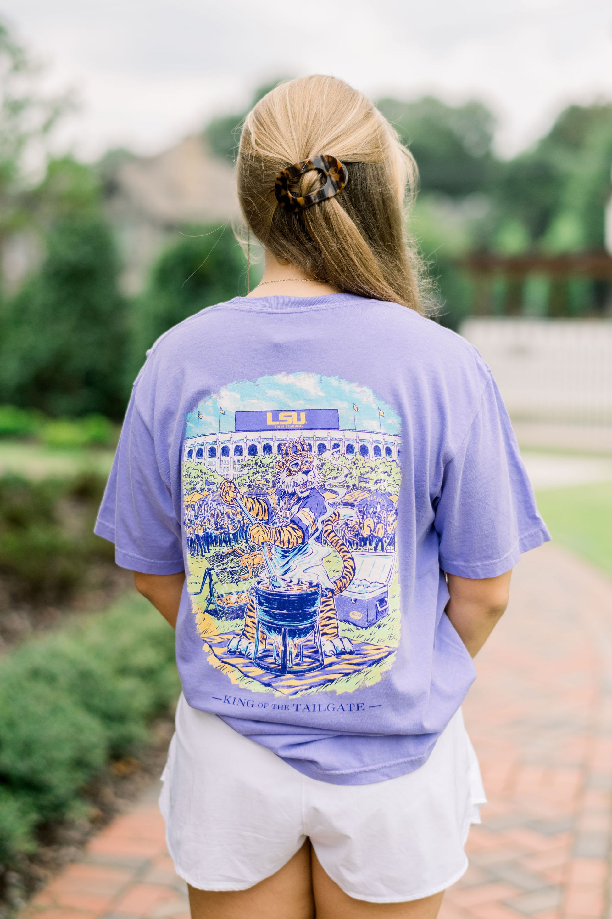 Louisiana State University Purple T-Shirt with an illustration of Mike the Tiger wearing a crown and stirring a pot of gumbo in front of the Tiger Stadium. Text “King of the Tailgate”