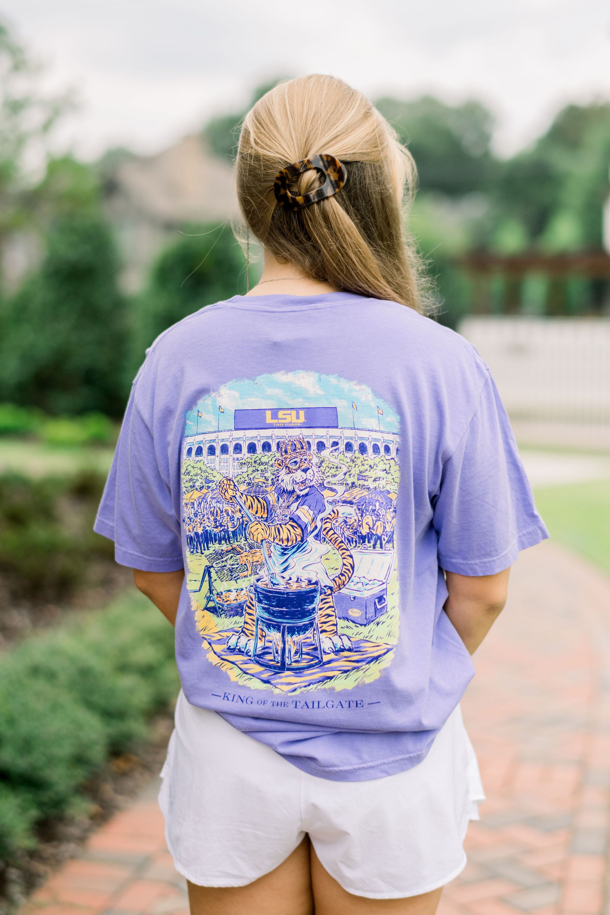 Louisiana State University Purple T-Shirt with an illustration of Mike the Tiger wearing a crown and stirring a pot of gumbo in front of the Tiger Stadium. Text “King of the Tailgate”
