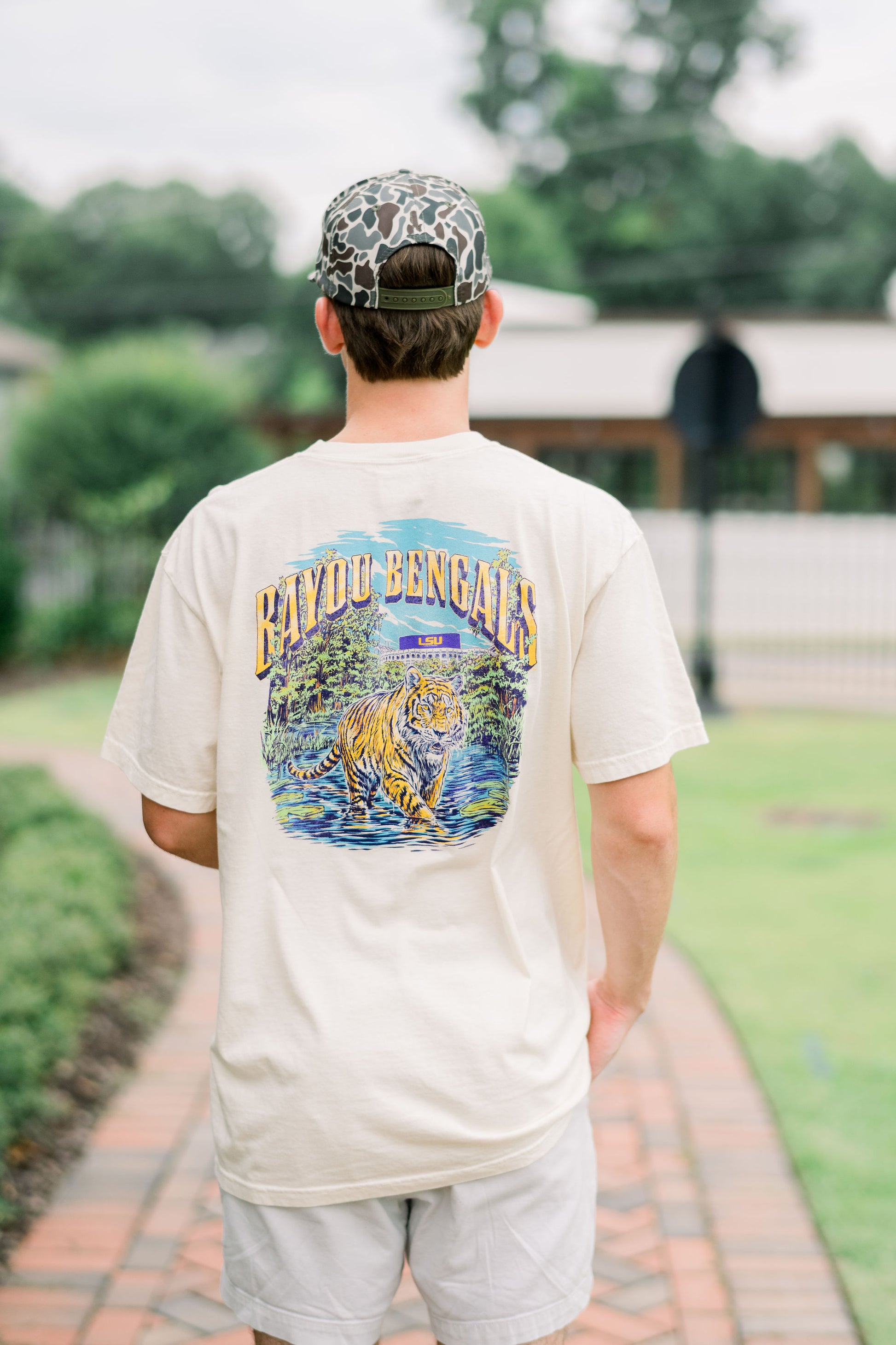 Louisiana State University Ivory T-Shirt with Gold Text “Bayou Bengals” over an illustration of a Bengal tiger prowling through the bayou with the Tiger stadium in the background